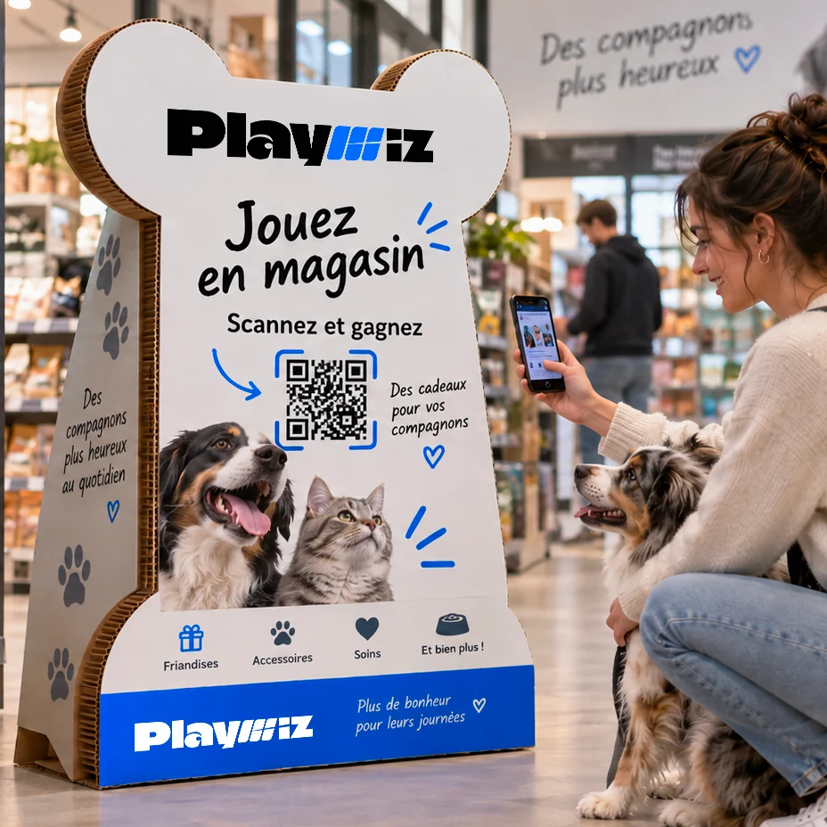 Une borne cartonnée découpée en forme d'os, dans une animalerie, dont une cliente scanne le QR code, son chien à côté d'elle