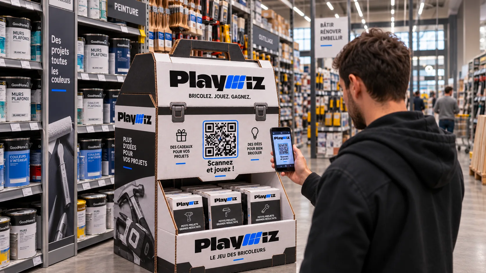 Une borne cartonnée en forme de caisse à outils, en rayon d'un magasin de bricolage, dont un client scanne le QR code