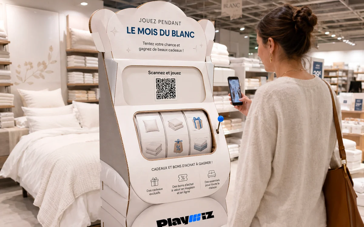 Une borne cartonnée en forme de machine à sous, aux couleurs d'une opération de linge de maison, dont une cliente scanne le QR code